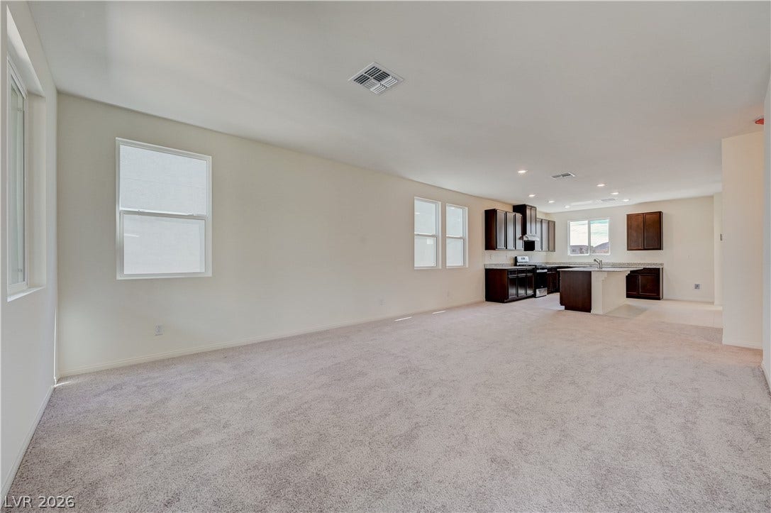 An open layout connects the carpeted living space to a fully equipped modern kitchen.