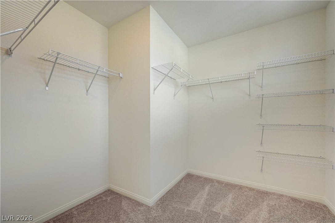 A spacious walk-in closet features ample wire shelving and comfortable wall-to-wall carpeting.