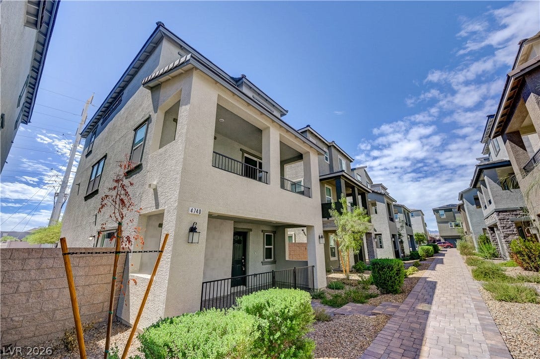Multi-level modern townhomes frame a paved pedestrian pathway under bright blue skies.