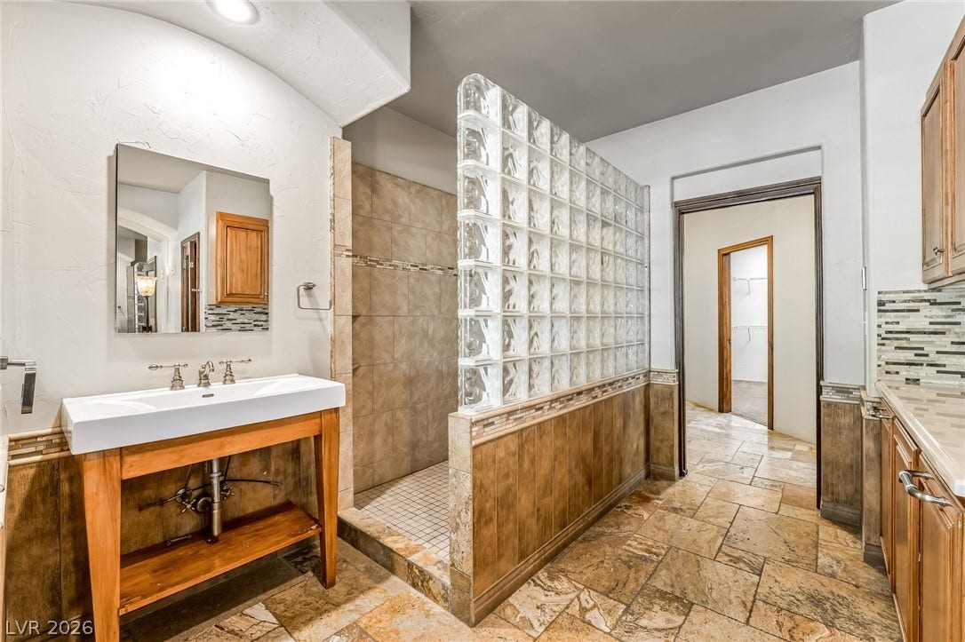 7154 Ranchito Circle, Las Vegas, NV 89120 Earth-toned floor tiles and a textured glass block partition wall define this spacious bathroom layout.