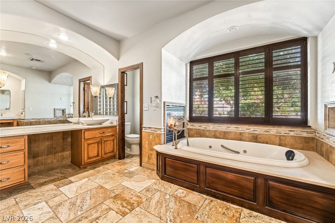 7154 Ranchito Circle, Las Vegas, NV 89120 Rich wood cabinetry and travertine tile flooring frame a deep soaking tub beneath arched architectural details.