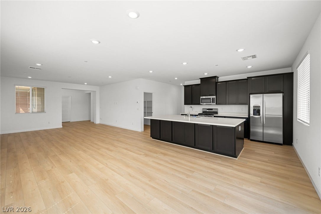 1670 Capri Falls Court, Henderson, NV 89011 Gleaming wood floors anchor an airy kitchen layout featuring dark cabinetry and light countertops.