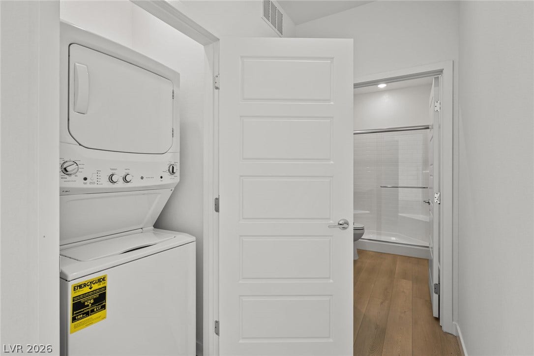 1670 Capri Falls Court, Henderson, NV 89011 A compact laundry nook features a stacked washer and dryer setup beside durable hardwood floors.