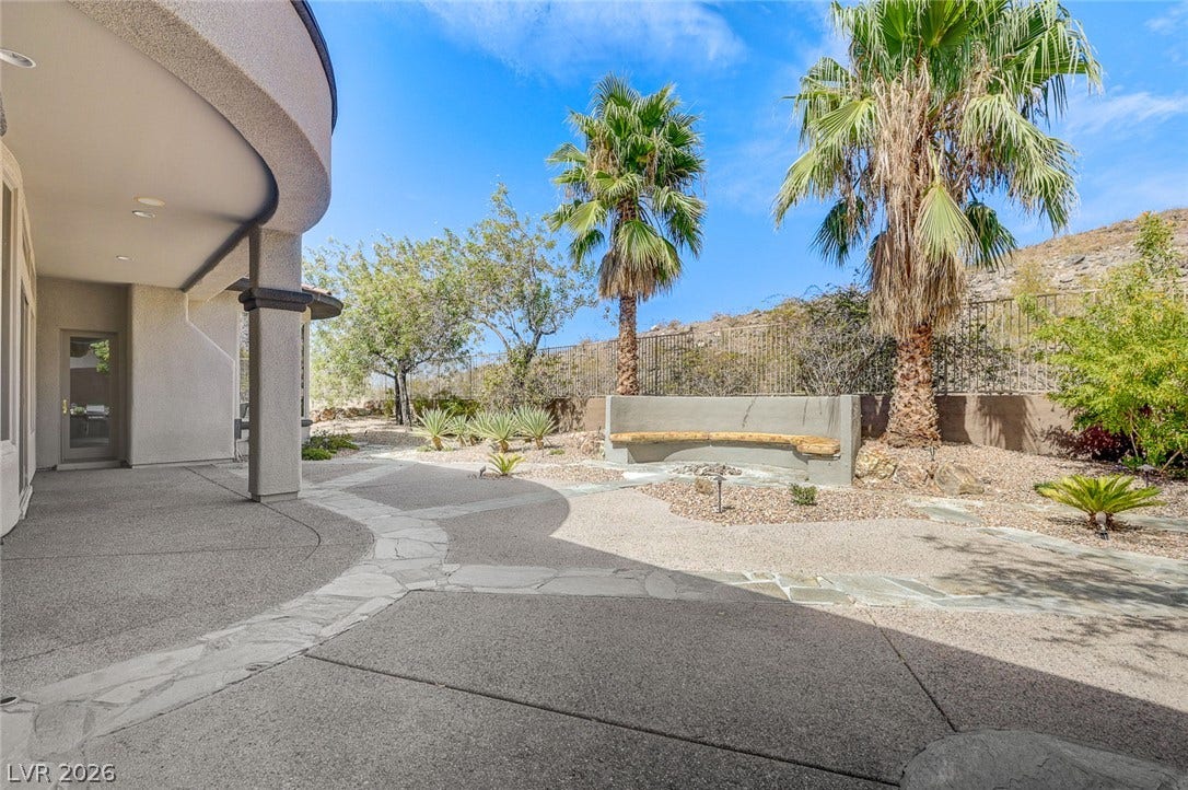8 Starbrook Drive, Henderson, NV 89052 A spacious concrete patio curves alongside a desert landscape framed by towering palm trees.