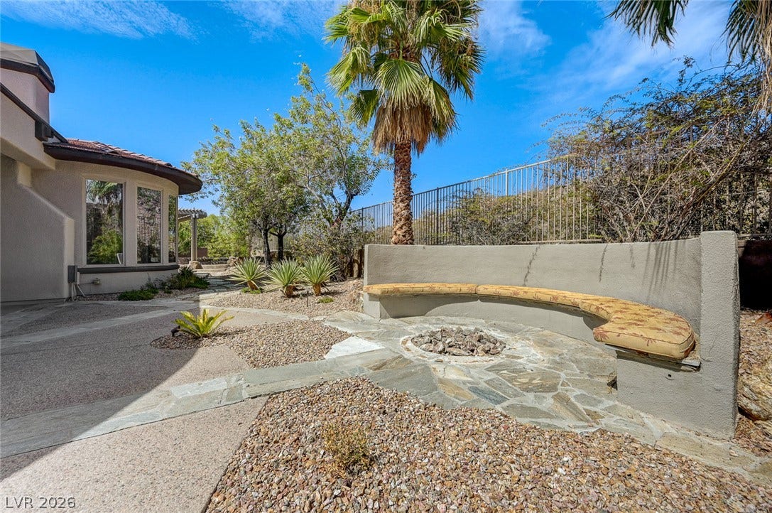 8 Starbrook Drive, Henderson, NV 89052 A curved built-in stone bench surrounds an outdoor fire pit within the landscaped backyard.