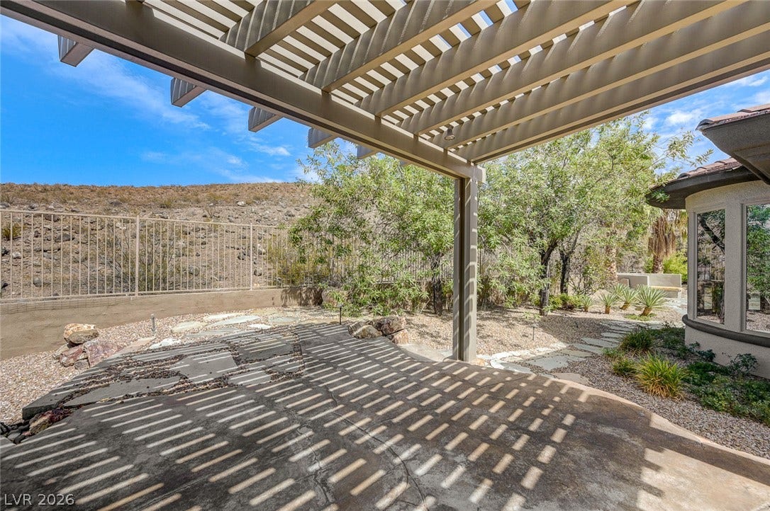 8 Starbrook Drive, Henderson, NV 89052 A spacious stone patio rests under a protective pergola overlooking the natural desert landscape.