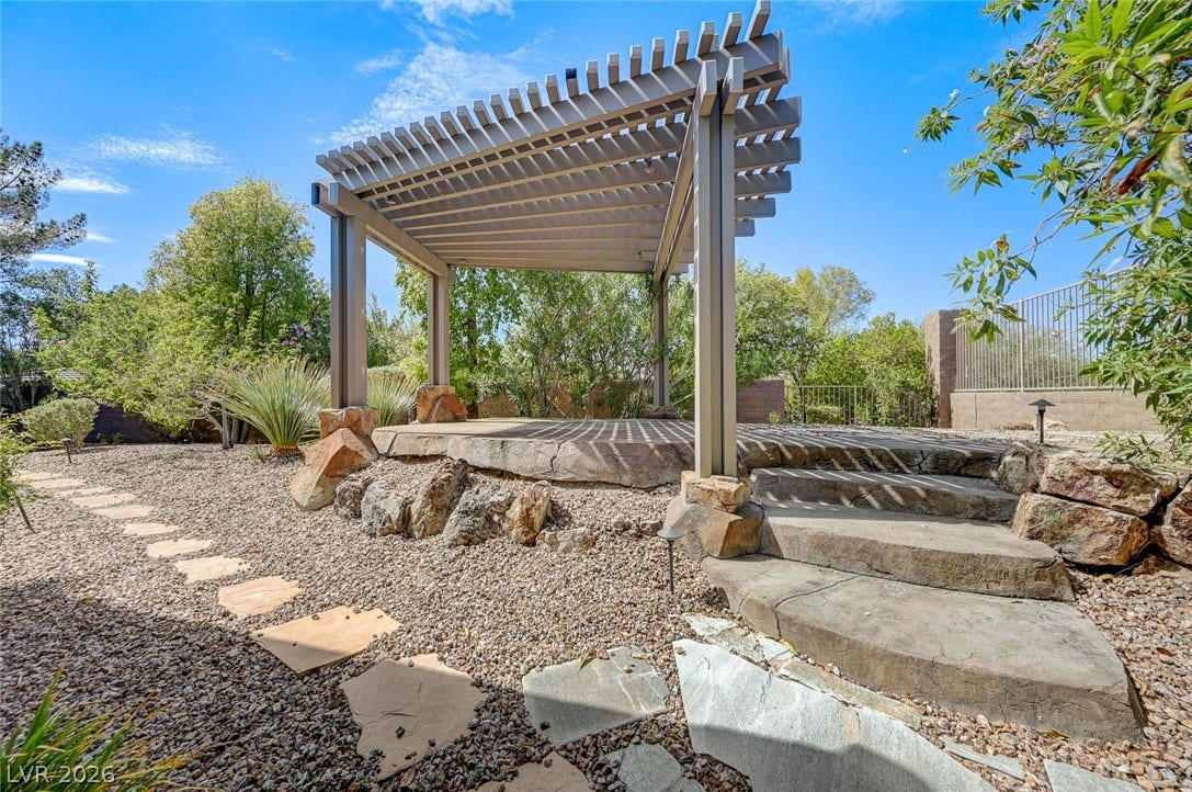 8 Starbrook Drive, Henderson, NV 89052 A custom wooden pergola shades a raised stone patio set within a landscaped desert yard.
