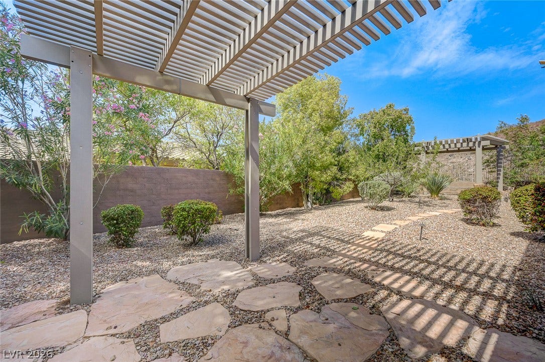 8 Starbrook Drive, Henderson, NV 89052 A shaded flagstone patio overlooks a low-maintenance gravel yard surrounded by mature greenery.