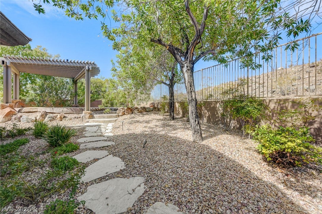 8 Starbrook Drive, Henderson, NV 89052 A stone pathway winds through low-maintenance landscaping beneath a wooden pergola structure.