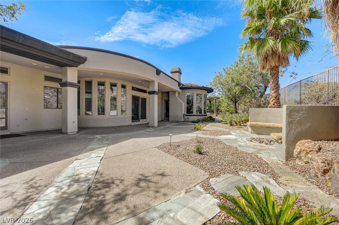 8 Starbrook Drive, Henderson, NV 89052 A spacious backyard features curved architectural lines and desert landscaping beneath sunny blue skies.