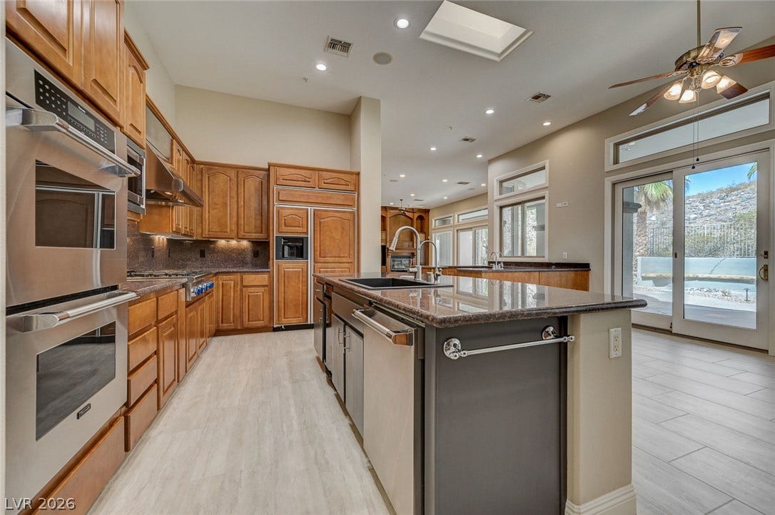 8 Starbrook Drive, Henderson, NV 89052 Gleaming stone countertops and warm wood cabinetry highlight a spacious, light-filled kitchen design.