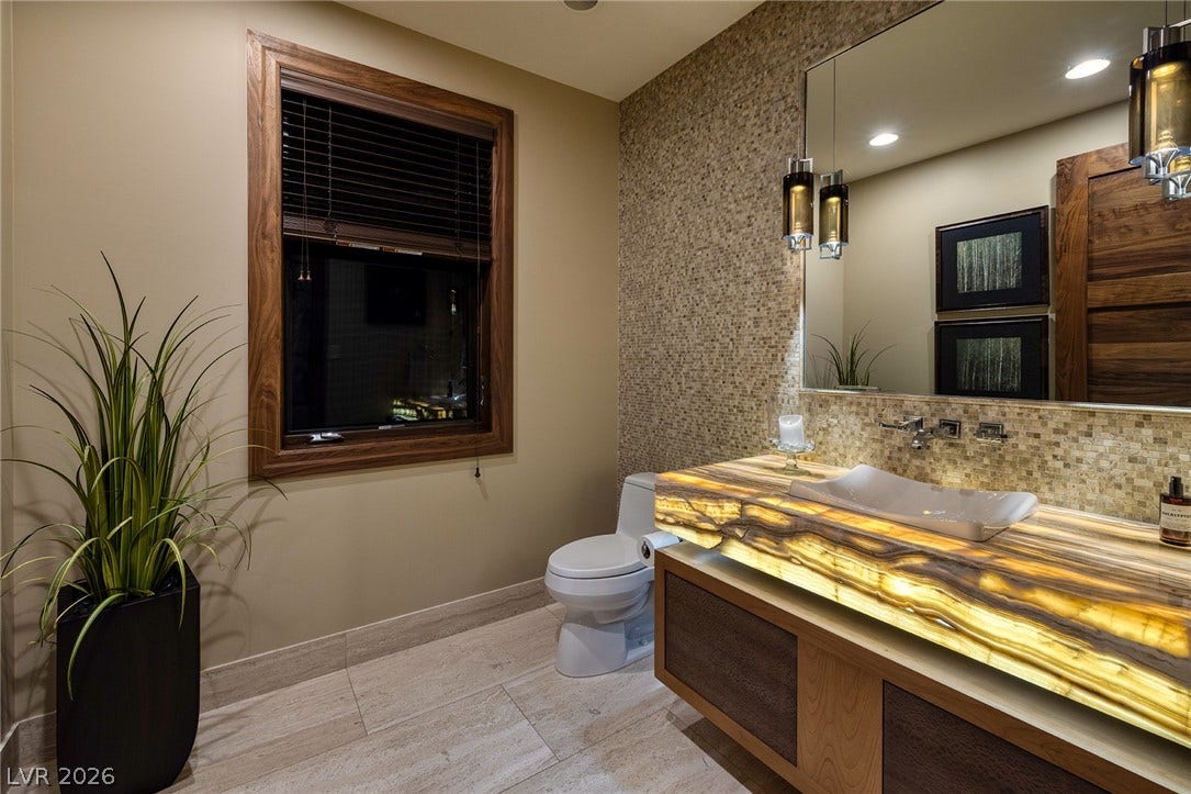 761 Dragon Ridge Drive, Henderson, NV 89012 An illuminated stone vanity pairs with mosaic tile accents in this modern bathroom.