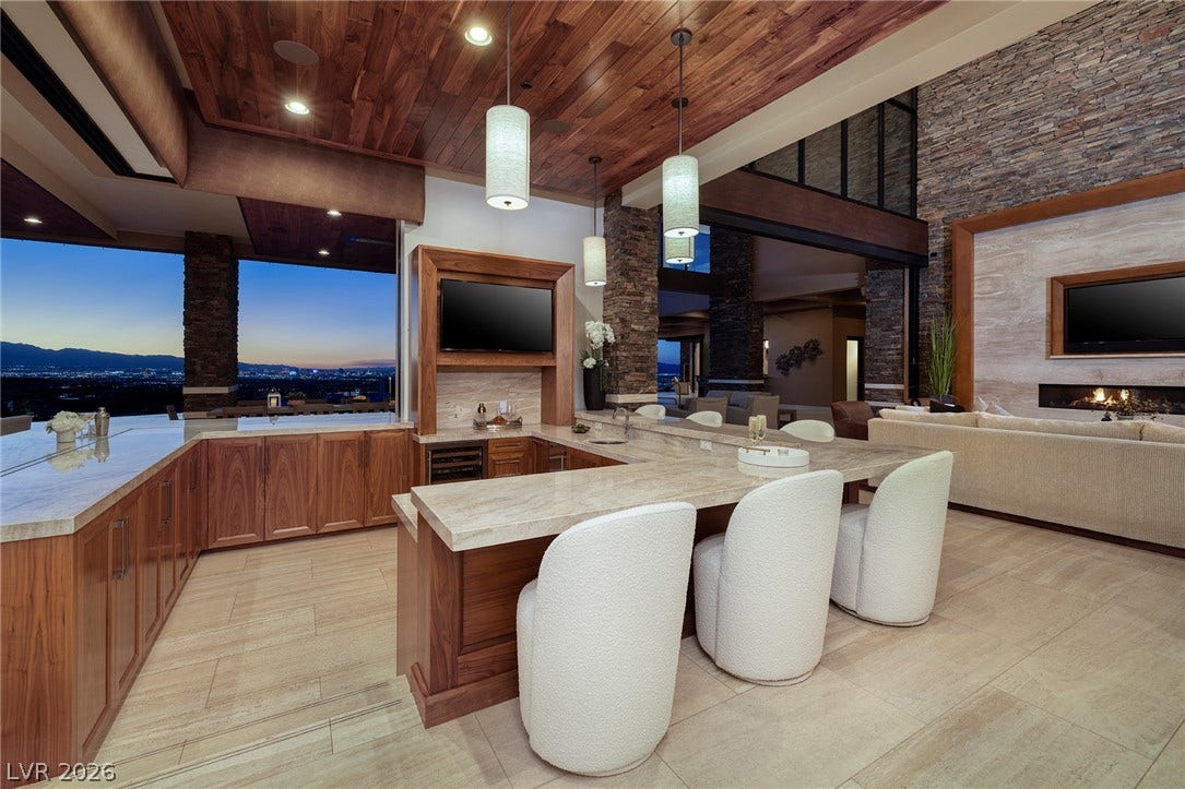 761 Dragon Ridge Drive, Henderson, NV 89012 Rich wood ceilings and stone accents frame a modern wet bar opening to mountain views.