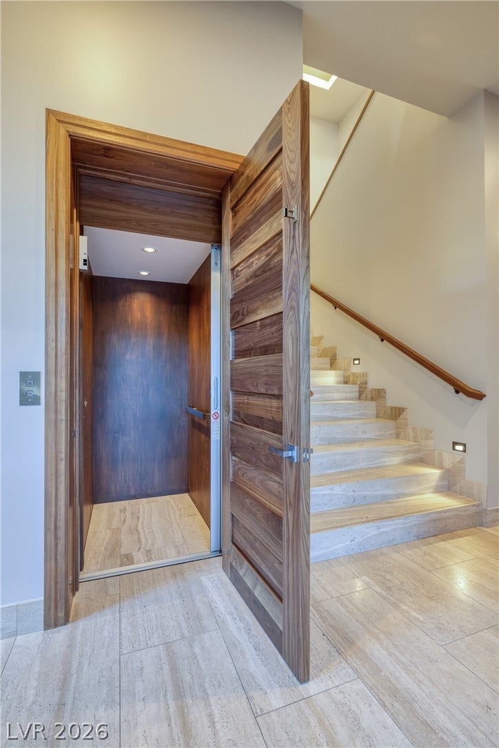 761 Dragon Ridge Drive, Henderson, NV 89012 Rich wood trim frames a residential elevator adjacent to a stone staircase.