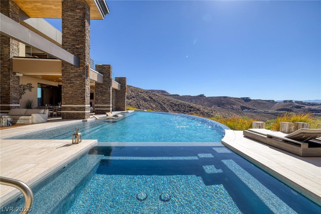 761 Dragon Ridge Drive, Henderson, NV 89012 An infinity pool and spa overlook wide desert hills under a clear blue sky.