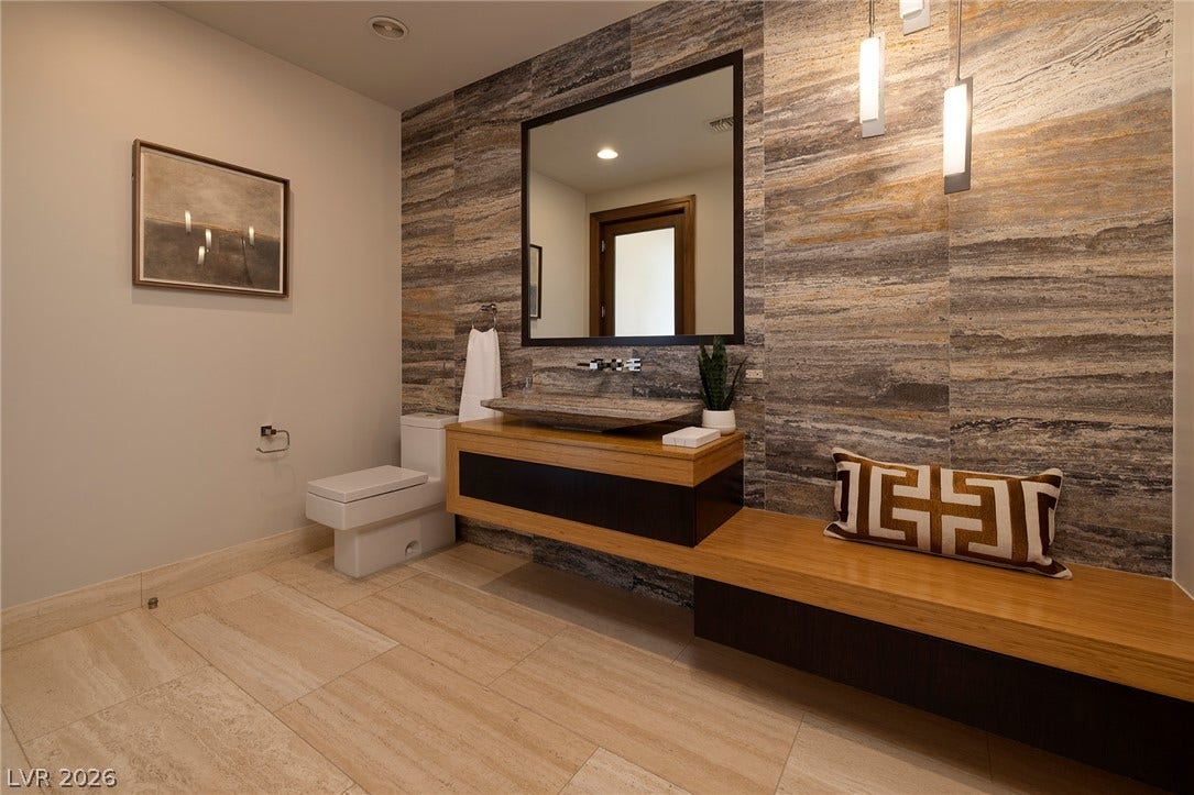 761 Dragon Ridge Drive, Henderson, NV 89012 Richly textured stone walls complement the floating timber vanity in this modern powder room.