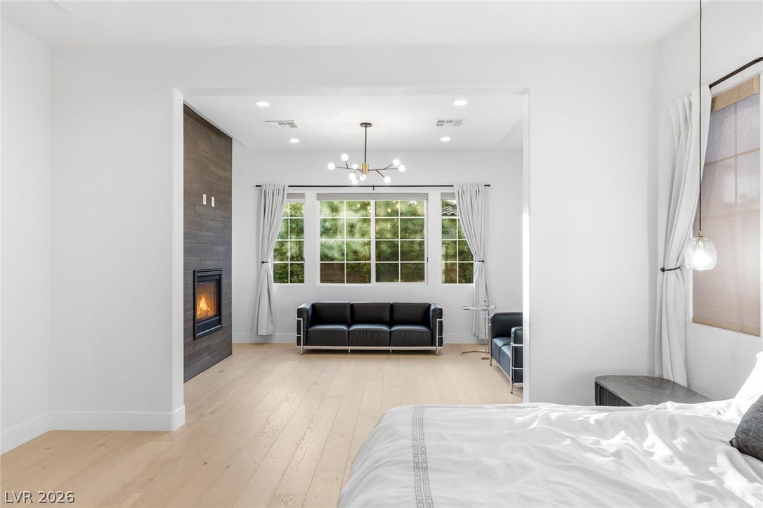 4078 San Franchesca Court, Las Vegas, NV 89141 A refined bedroom features a contemporary fireplace and abundant natural light from large windows overlooking greenery.