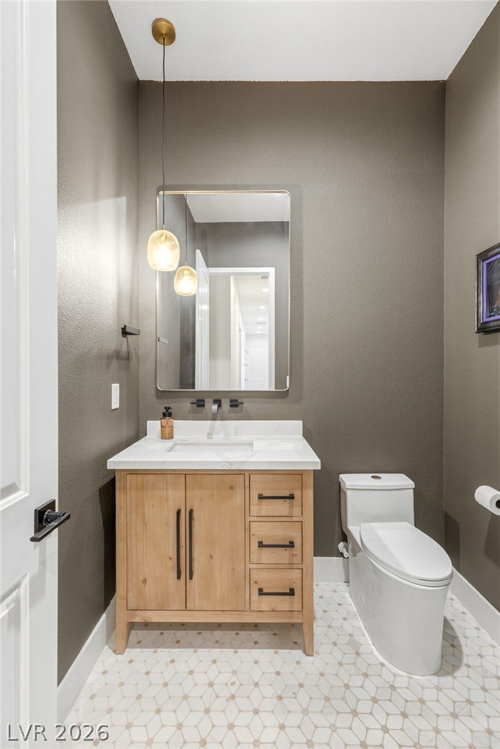 4078 San Franchesca Court, Las Vegas, NV 89141 A well-appointed powder room features a natural wood vanity, a stylish mirror, and a unique tiled floor.