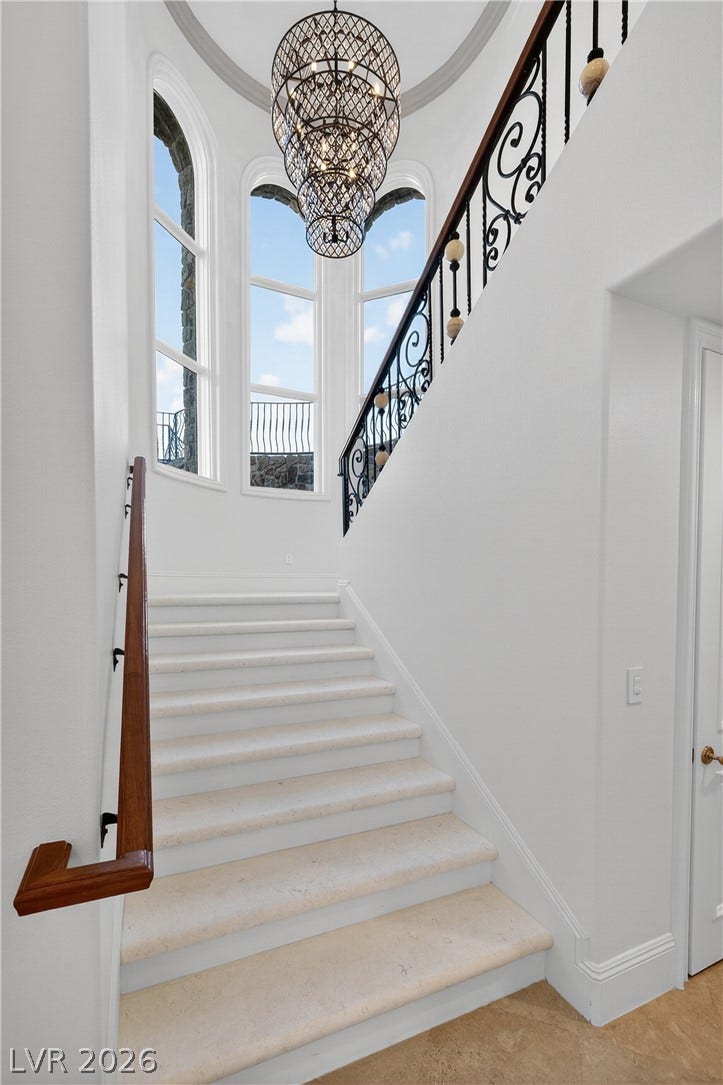 4 Ayden Drive, Henderson, NV 89052 An elegant stone staircase ascends past towering windows beneath a soaring tray ceiling.