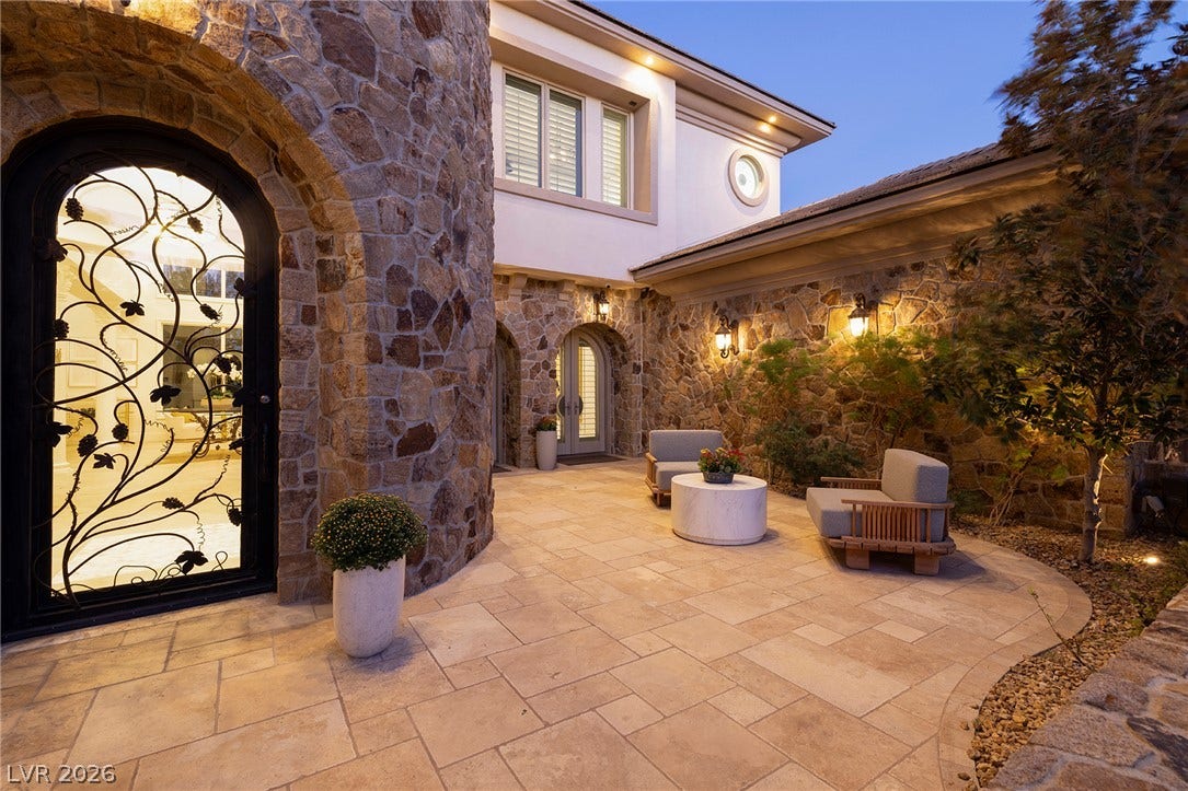 4 Ayden Drive, Henderson, NV 89052 Stone walls and a paved terrace create a classic courtyard entrance beneath the twilight sky.