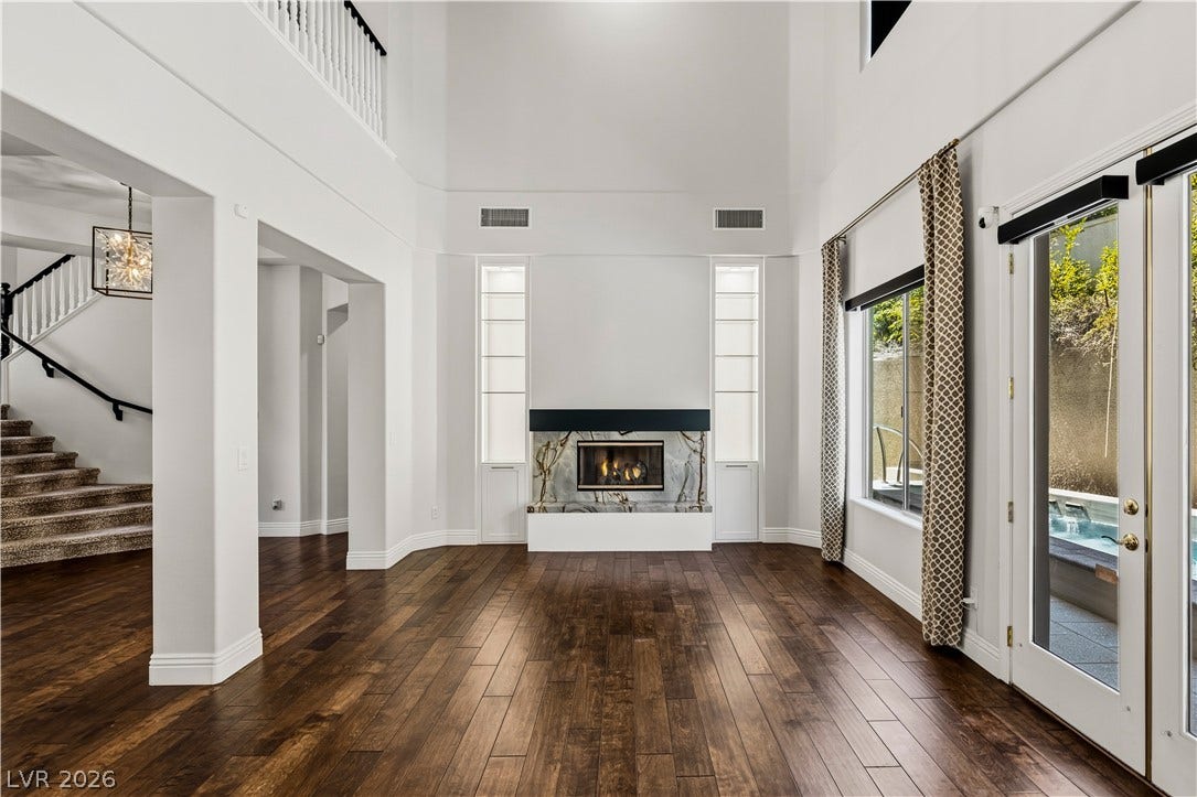 1201 Mersault Court, Las Vegas, NV 89144 Formal Living Room. Rich hardwood flooring complements the towering ceilings and minimalist fireplace in this airy space.