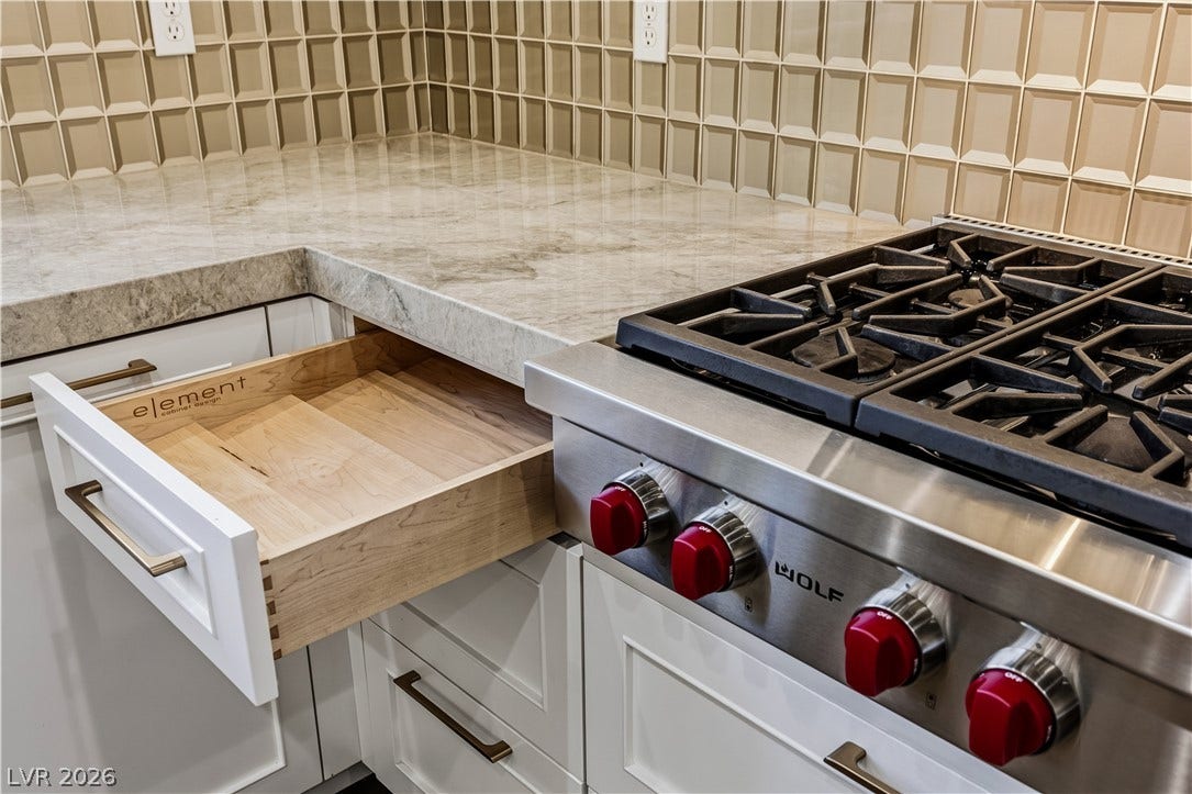 1201 Mersault Court, Las Vegas, NV 89144 Gleaming stone countertops flank a professional gas cooktop featuring signature red control knobs.