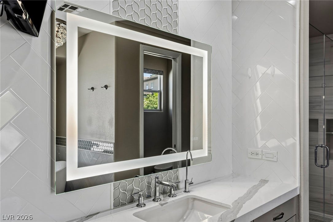 1201 Mersault Court, Las Vegas, NV 89144 Herringbone wall tile and a modern illuminated mirror elevate this stylish vanity area.