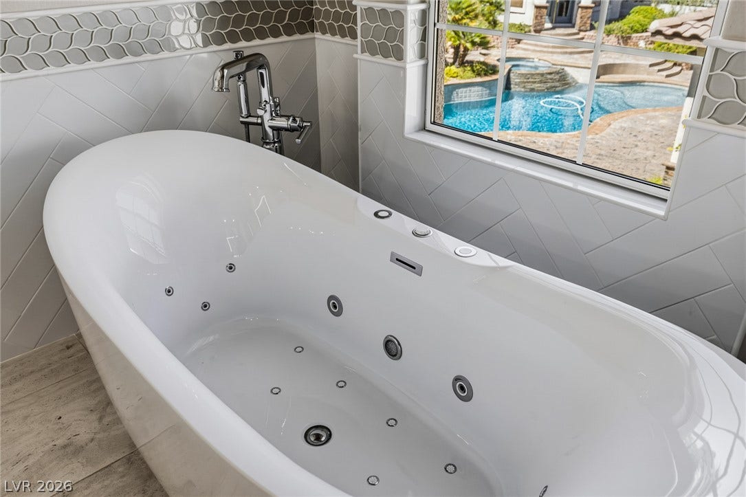 1201 Mersault Court, Las Vegas, NV 89144 An elegant soaking tub with jets stands beside a large window overlooking the backyard pool.