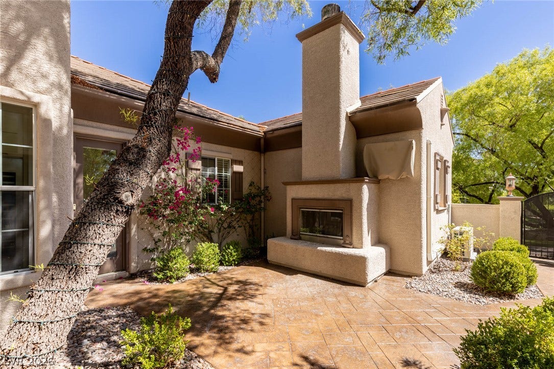 1201 Mersault Court, Las Vegas, NV 89144 An inviting outdoor fireplace warms this stucco patio area surrounded by mature greenery.