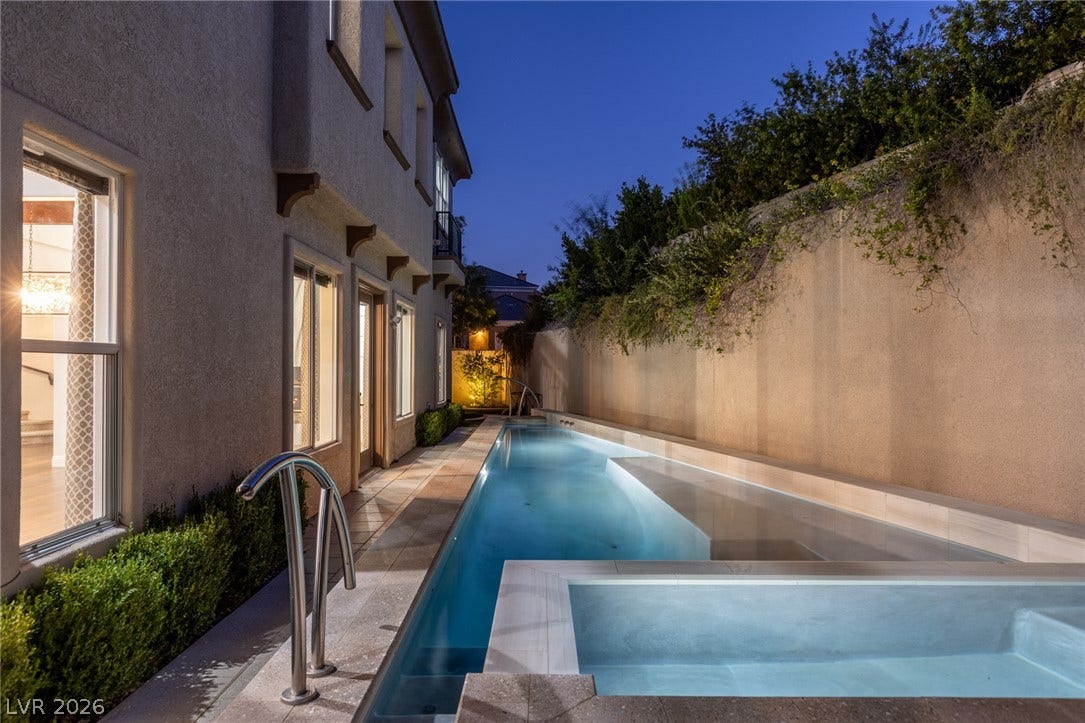 1201 Mersault Court, Las Vegas, NV 89144 An elongated lap pool stretches alongside the stucco exterior under an evening sky.