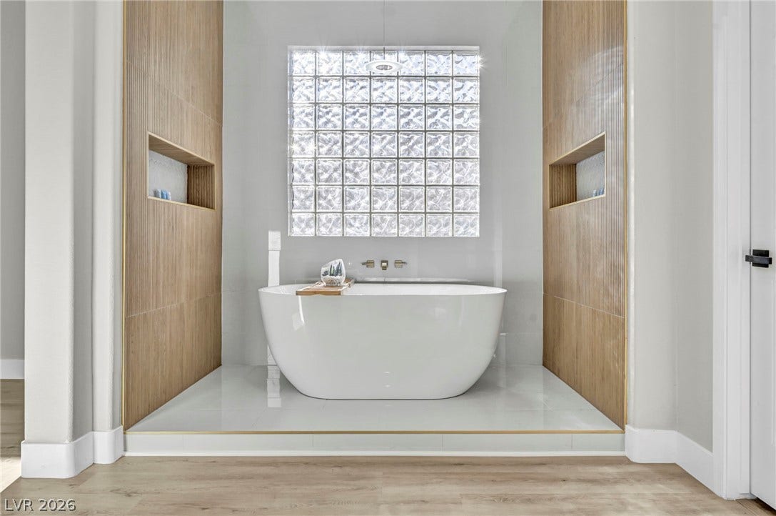 17 Winding Road, Henderson, NV 89052 Modern freestanding tub centers a symmetric alcove framed by warm wood paneling and glass block windows.