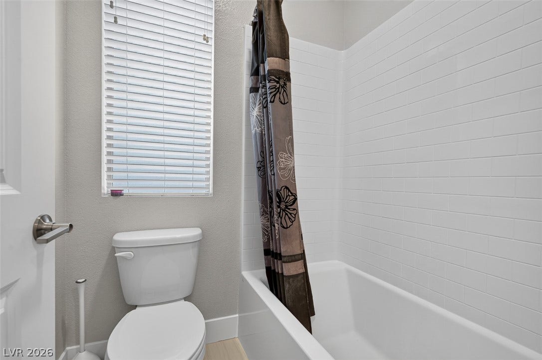 6849 Desert Finch Street, North Las Vegas, NV 89084 White subway tile surrounds the built-in bathtub beneath a window with horizontal blinds.