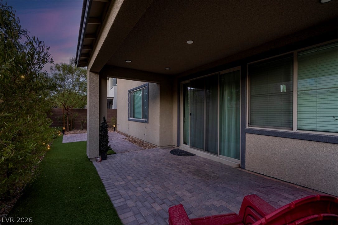 6849 Desert Finch Street, North Las Vegas, NV 89084 A covered paver patio opens to a manicured grassy yard under a twilight sky.