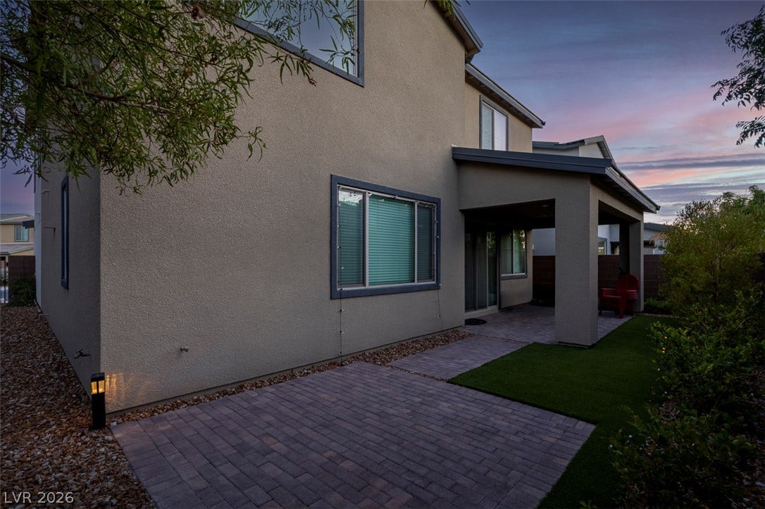 6849 Desert Finch Street, North Las Vegas, NV 89084 A twilight view reveals a covered rear patio featuring interlocking pavers and manicured turf.