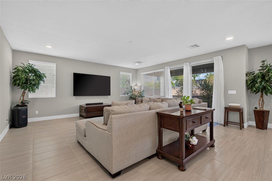 6849 Desert Finch Street, North Las Vegas, NV 89084 An open living area features neutral tiled flooring and extensive window glass leading outdoors.