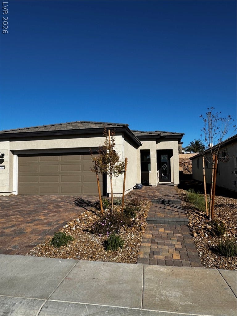 162 Palm Fox Court, Henderson, NV 89011 A paved walkway leads past desert landscaping to the glass-paneled front entrance of this modern home.
