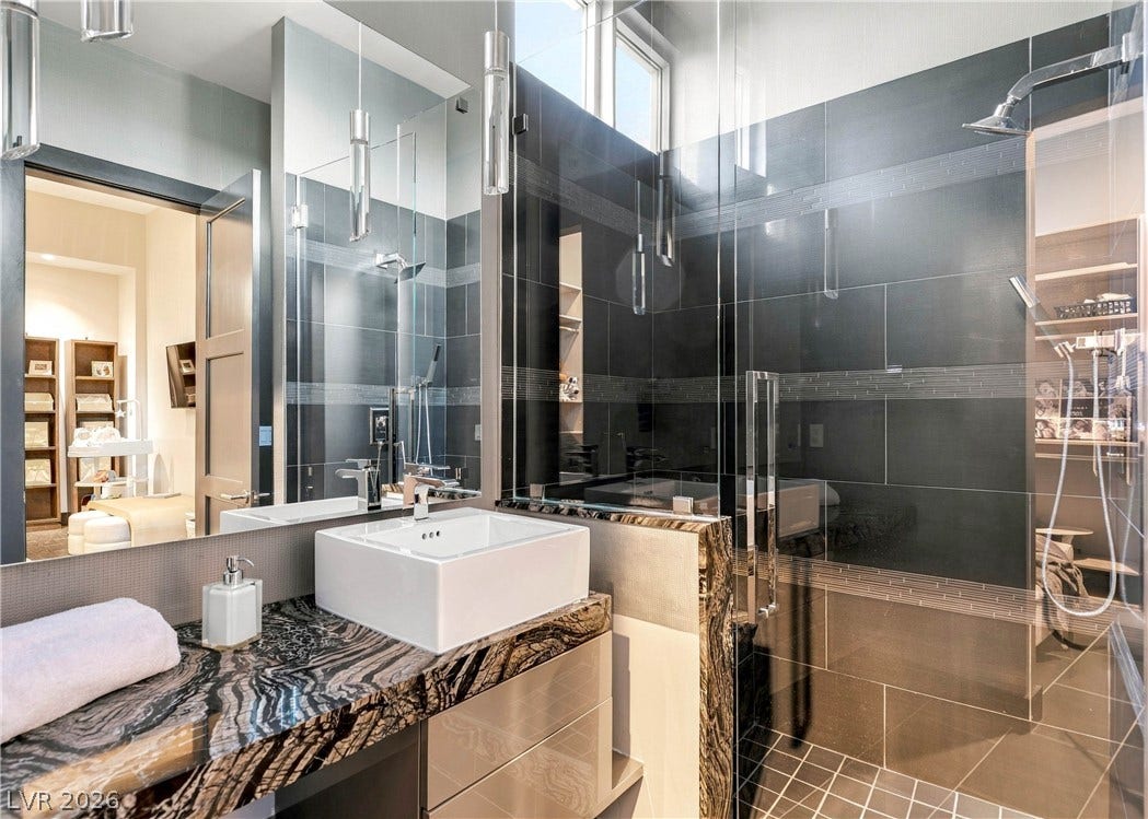 3716 Caesars Circle, Las Vegas, NV 89120 Dramatic dark tiling and matching stone countertops elevate this contemporary bathroom design.