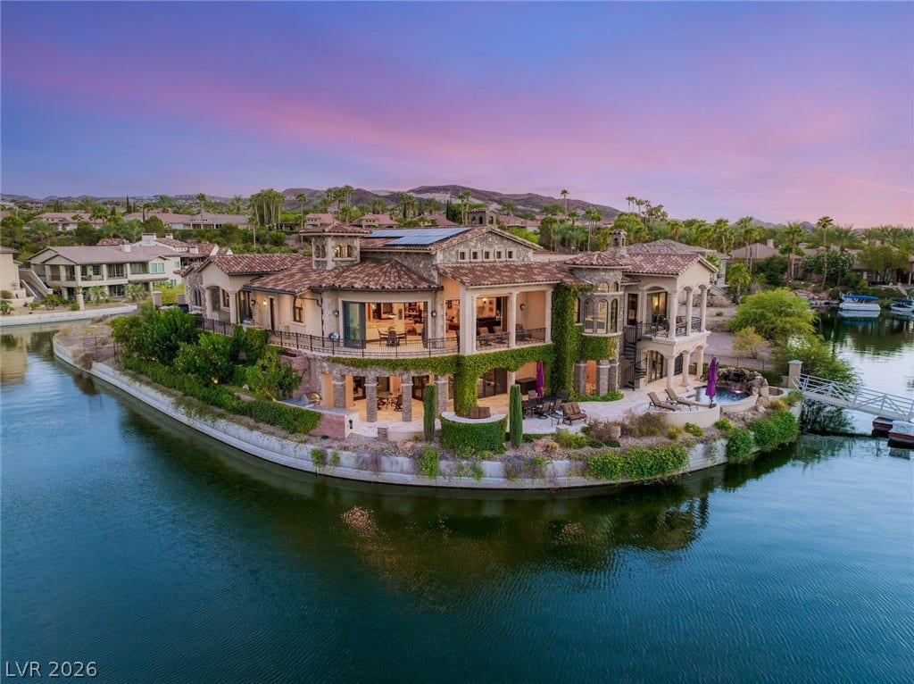 7 Lido Nord, Henderson, NV 89011 Dramatic waterfront curves frame this expansive stone estate surrounded by tranquil lake waters under sunset skies.