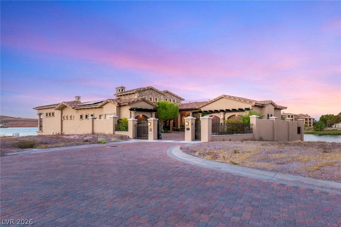 7 Lido Nord, Henderson, NV 89011 An elegant stone and stucco estate boasts a paver driveway under a vibrant twilight sky.