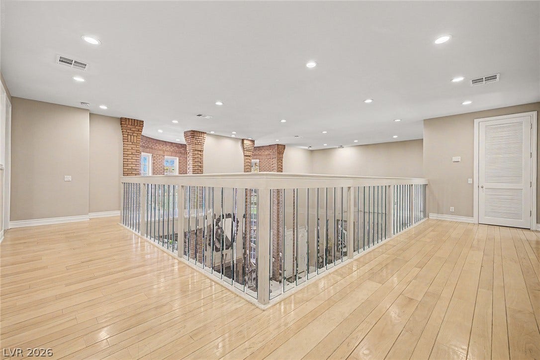 1105 Broadmoor Avenue, Las Vegas, NV 89109 A spacious upper-level landing overlooks the lower floor, showcasing hardwood flooring and exposed brick columns.