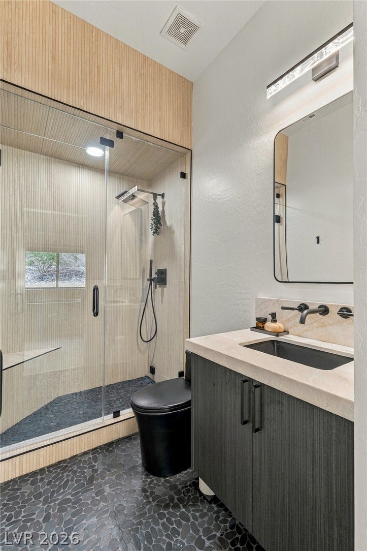 40 Stonemark Drive, Henderson, NV 89052 Pebble tile flooring complements a modern glass-enclosed shower and contemporary vanity in this sleek bathroom.