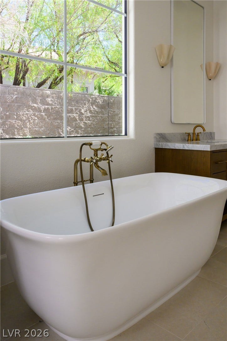 12007 Oakland Hills Drive, Las Vegas, NV 89141 An elegant freestanding soaking tub rests beside a large picture window framed by stone counters.