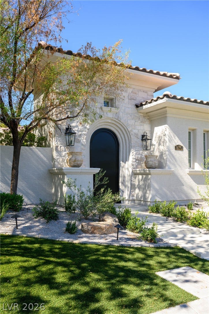 12007 Oakland Hills Drive, Las Vegas, NV 89141 An arched entry door sits within a stone-accented facade under a classic tiled roof.