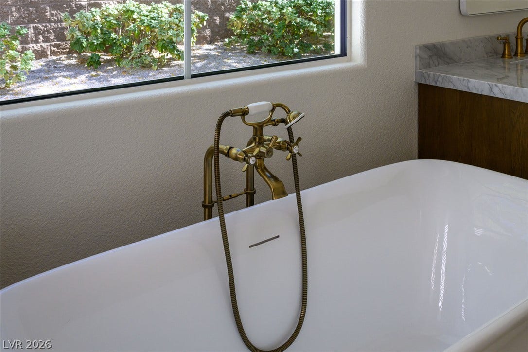 12007 Oakland Hills Drive, Las Vegas, NV 89141 A freestanding soaking tub sits beneath a wide window looking out onto the garden.