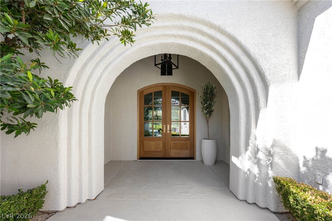 12007 Oakland Hills Drive, Las Vegas, NV 89141 An arched entryway features stucco walls and double wood doors leading into the home.