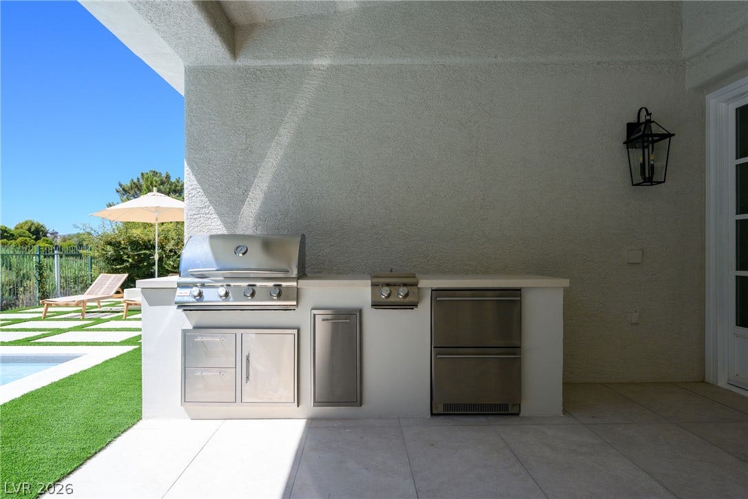 12007 Oakland Hills Drive, Las Vegas, NV 89141 A shaded outdoor kitchen features stone countertops alongside a built-in grill and stainless steel drawers.