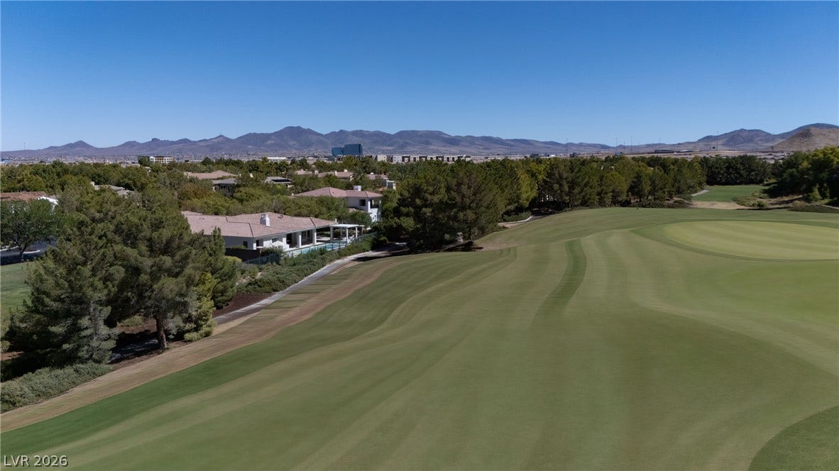 12007 Oakland Hills Drive, Las Vegas, NV 89141 Lush fairways stretch toward distant mountain peaks under a clear blue sky.