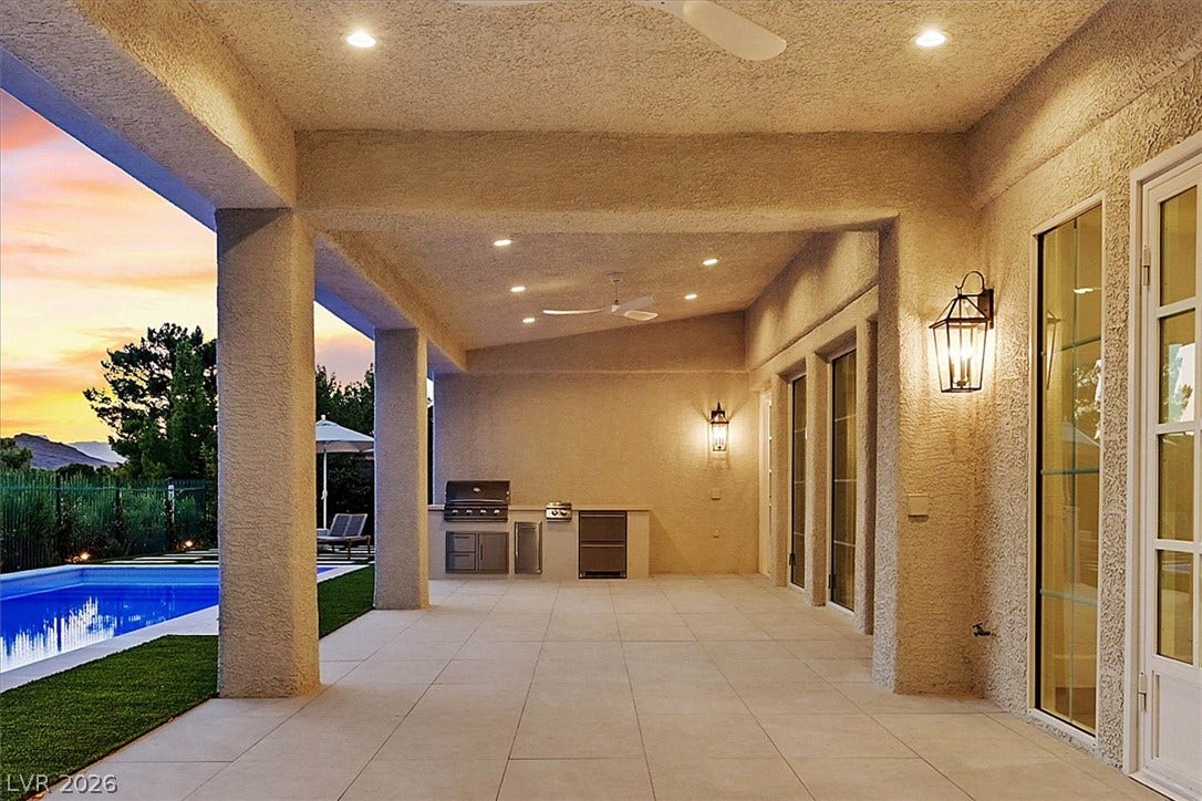 12007 Oakland Hills Drive, Las Vegas, NV 89141 An expansive covered stone patio steps out to a glistening swimming pool at twilight.