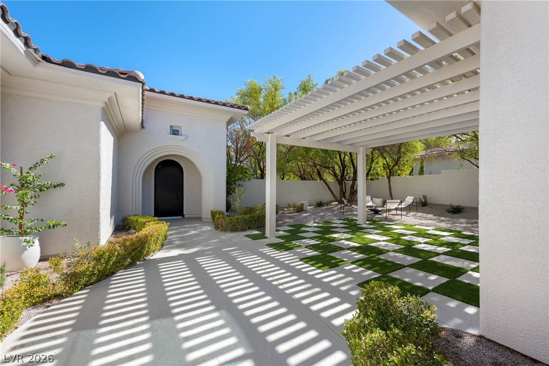 12007 Oakland Hills Drive, Las Vegas, NV 89141 An elegant stucco exterior frames a paved pathway leading to a modern pergola structure.