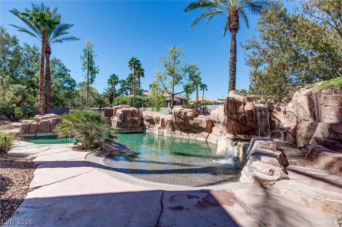 9916 Aspen Knoll Court, Las Vegas, NV 89117 Towering palms and a stone-lined pool create a private desert oasis under clear blue skies. Fountains and beach entry.